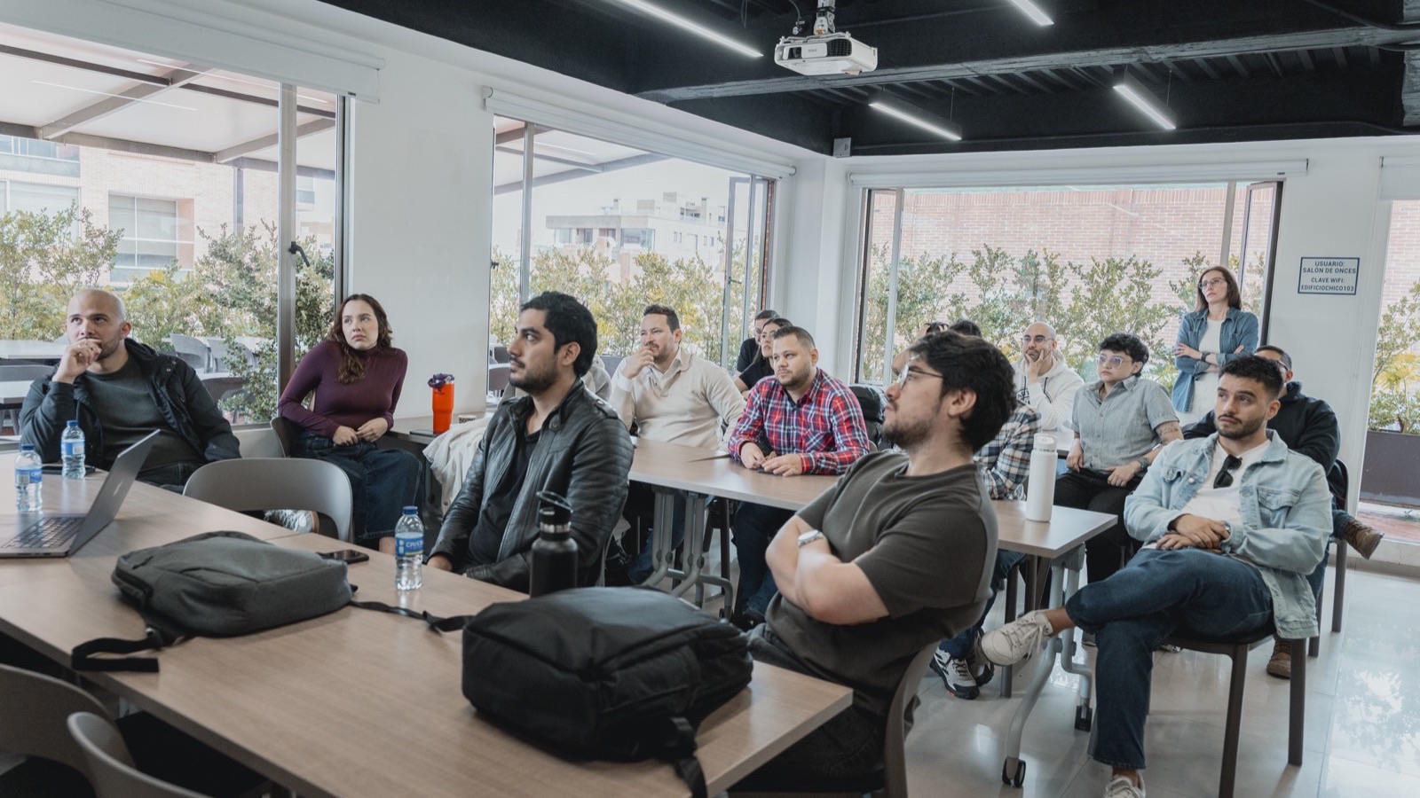Leanware engineers seated at desks in their Bogotá, Colombia office during an in-person all-hands session, listening to a teammate present from the front of the room